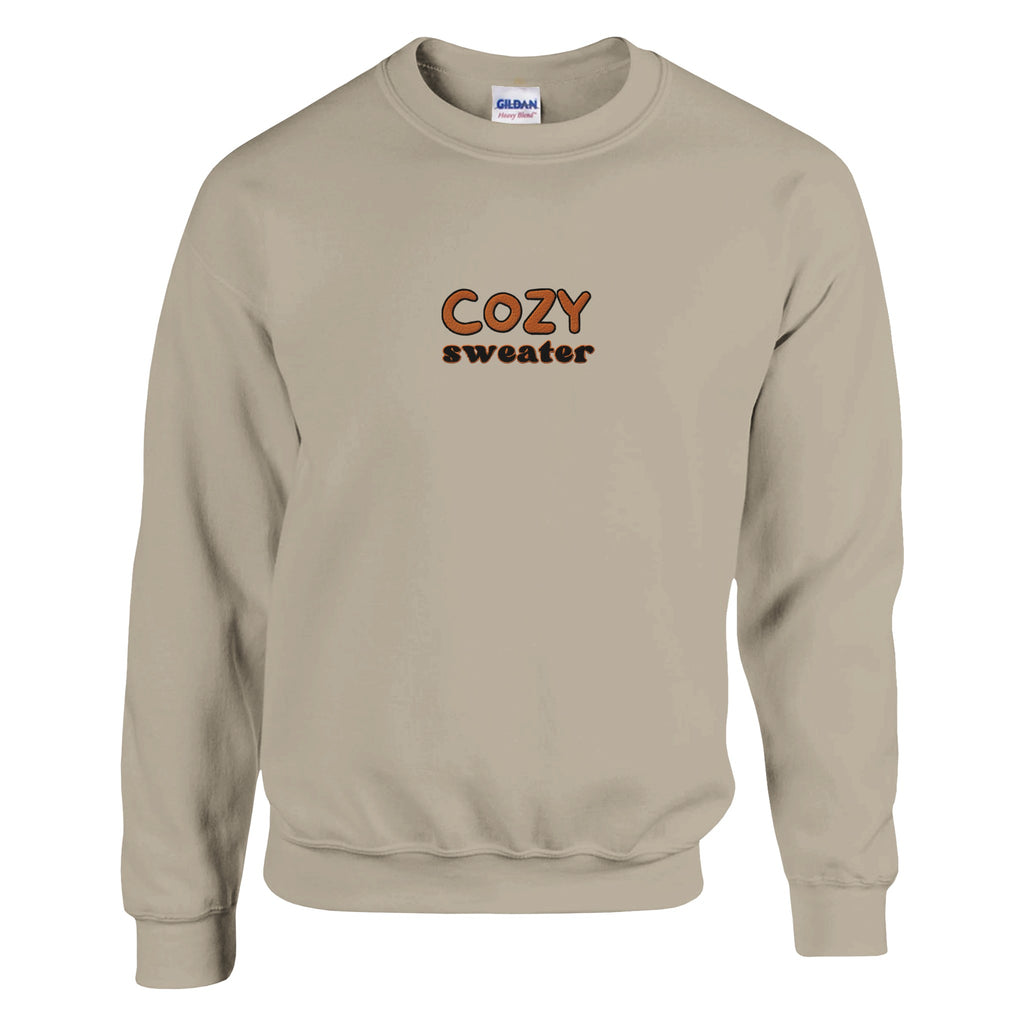 Beige sweatshirt from the unisex Cozy Sweater collection, featuring the "COZY sweater" design in brown and orange embroidery on the front, crafted from ultra-soft premium fabric.